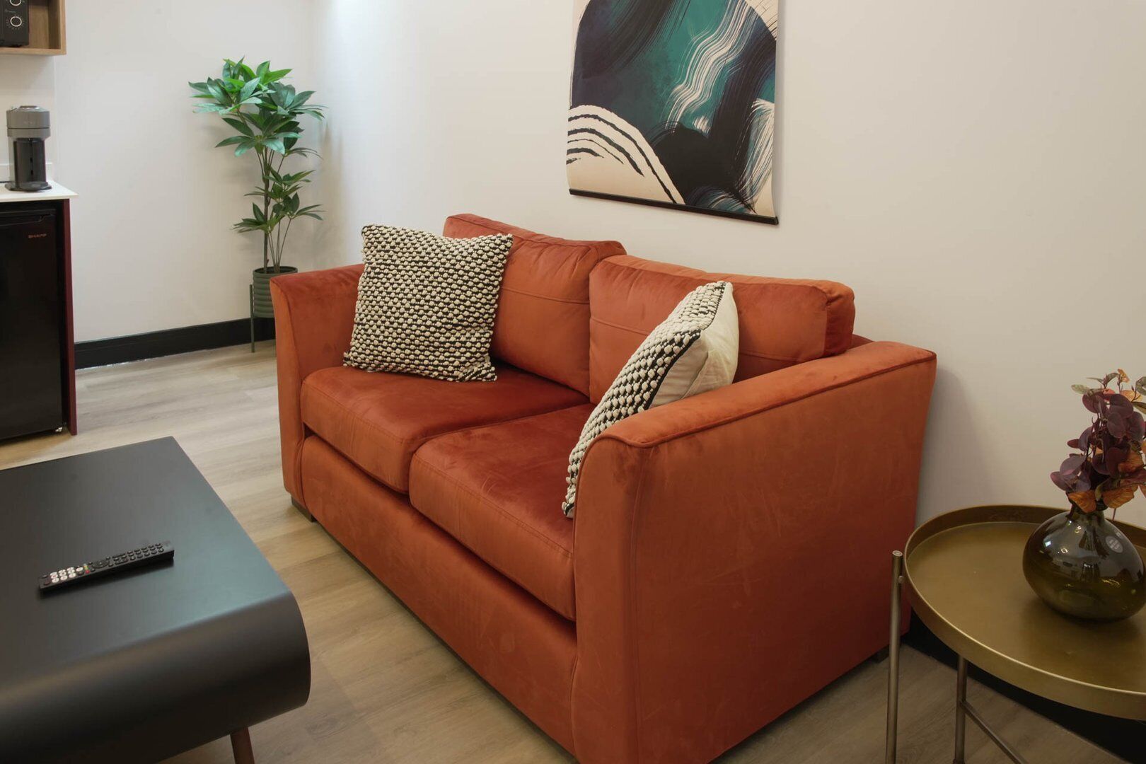 Een moderne woonkamer met een rode bank, een zwarte salontafel en een kleine ronde tafel met een vaas.
