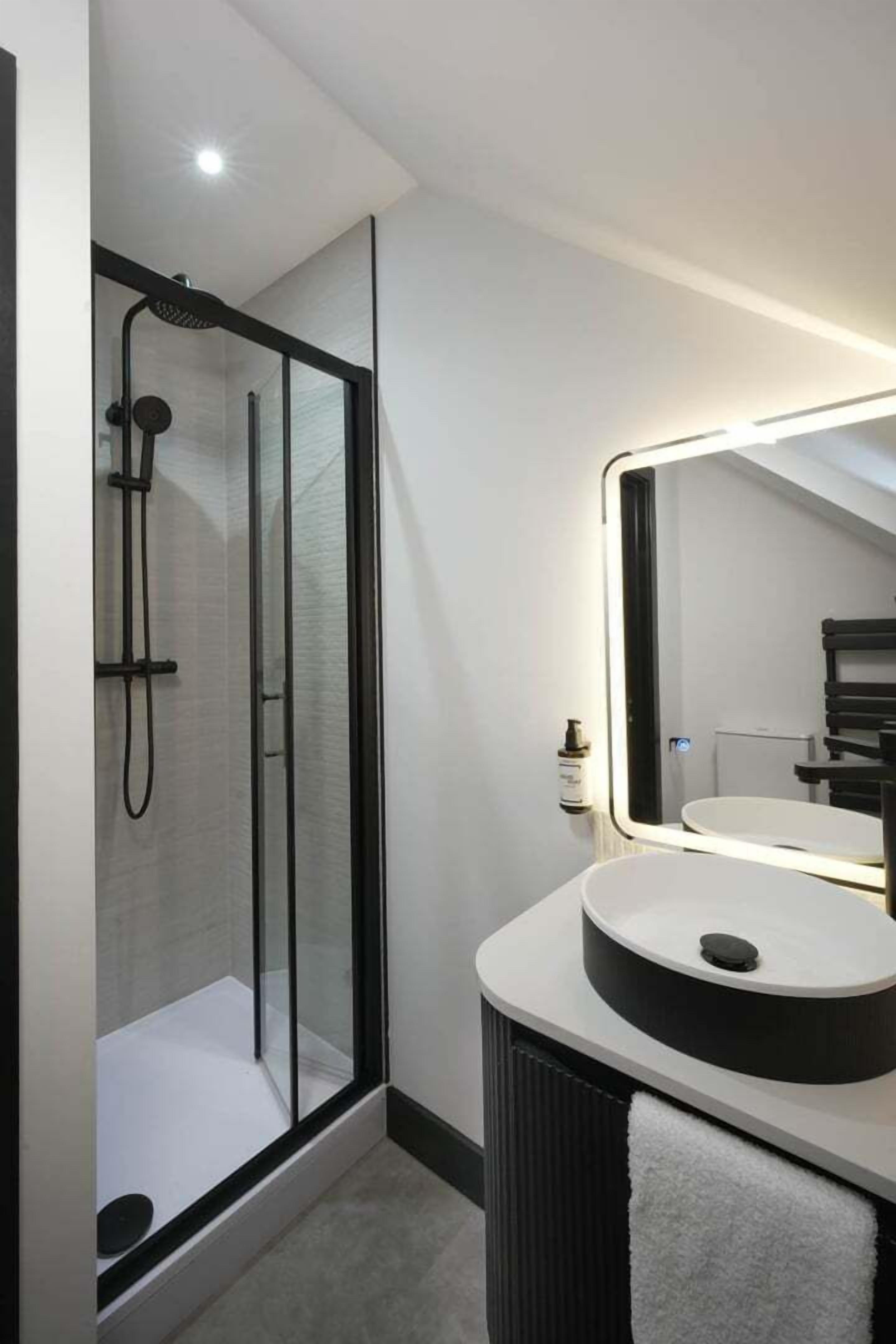 A modern bathroom with a glass-enclosed shower, a round sink with a mirror, and a towel rack.