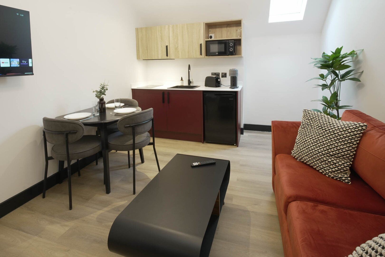 A compact living space with a dining area, kitchenette, and a sofa with a patterned cushion.