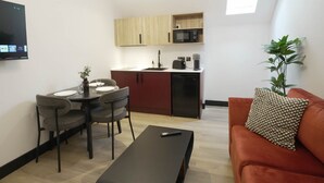 A compact living space with a dining area, kitchenette, and a sofa with a patterned cushion. - Sixty Aparthotel 2bed, Central Cardiff + Parking (Cardiff)