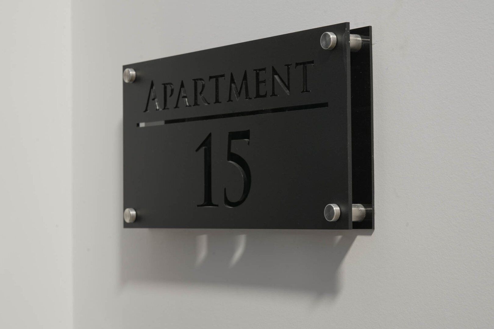 Ein schwarzes Metallschild mit der Aufschrift "APARTMENT 15", das an einer Wand befestigt ist.
