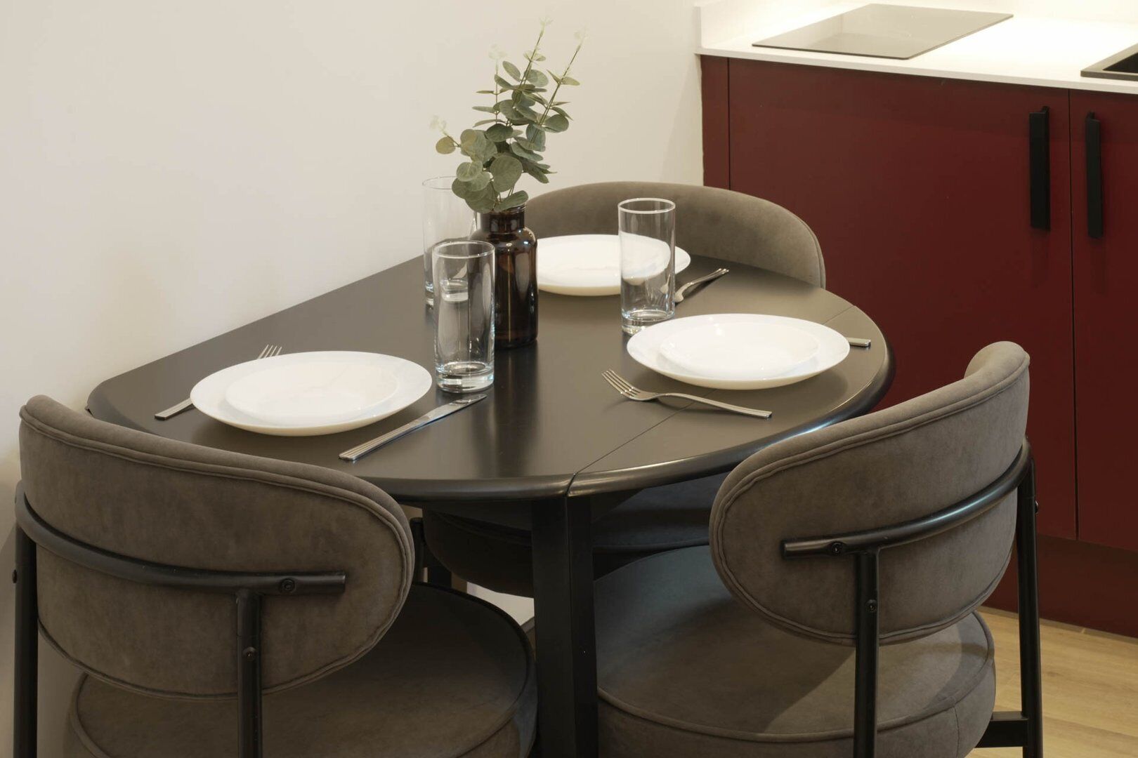 A dining table with four chairs, a vase with a plant, and two glasses.