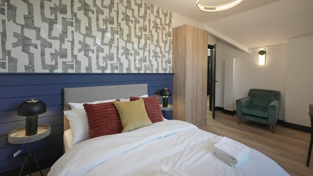 Ein modernes Hotelzimmer mit einem großen Bett, zwei Nachttischlampen, einem grünen Sessel und einer Wand mit Muster.