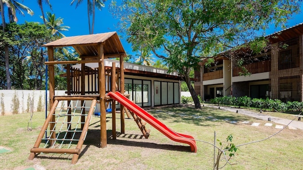 Un parque infantil con un tobogán y una estructura para escalar, rodeado de césped y árboles.