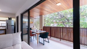 Un balcón moderno con techo de madera, una mesa de comedor con sillas y un refrigerador.
