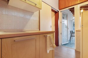 Une cuisine dotée de meubles de rangement en bois, d’un plan de travail et d’une porte-fenêtre coulissante donnant sur un espace extérieur.