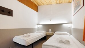 Ein Hotelzimmer mit zwei Einzelbetten, einem Nachttisch mit Lampe und einer Holzbalkendecke.