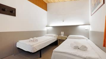 Camera d'albergo con due letti singoli, un comodino con una lampada e un soffitto in legno.