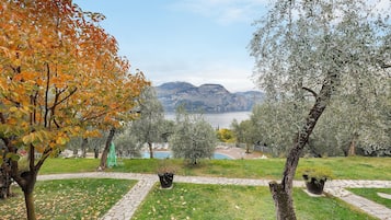 Un parco con un sentiero in pietra, alberi con foglie autunnali e vista su montagne e un lago.