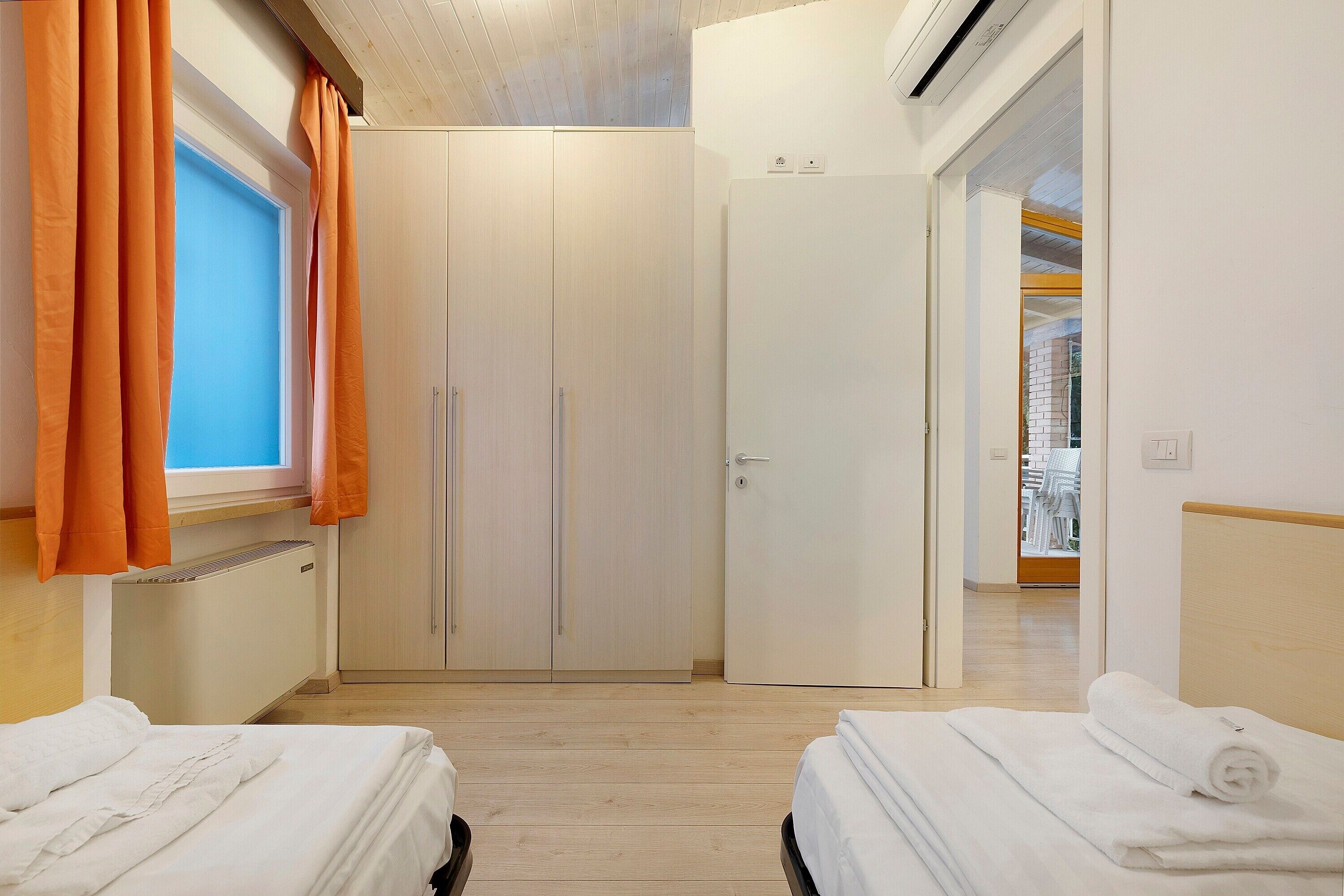 A hotel room with two beds, a wardrobe, a radiator, and an air conditioning unit.