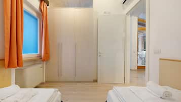 A hotel room with two beds, a wardrobe, a radiator, and an air conditioning unit.