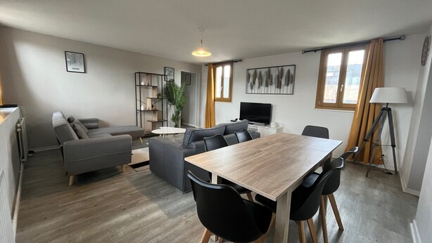 Una sala moderna con una mesa de comedor de madera, sofás grises y una televisión.