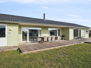 Ein eingeschossiges Haus mit überdachter Terrasse, Schornstein und einer Holzterrasse.