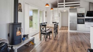 A modern kitchen with a wood-burning stove, a dining area with chairs, and a view through a glass door to the outside. - 5 Star Holiday Home in Sydals (Sydals)