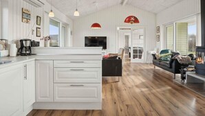 A spacious living area with a large wooden floor, a central island with white cabinetry, a black sofa, and a fireplace. - 5 Star Holiday Home in Sydals (Sydals)