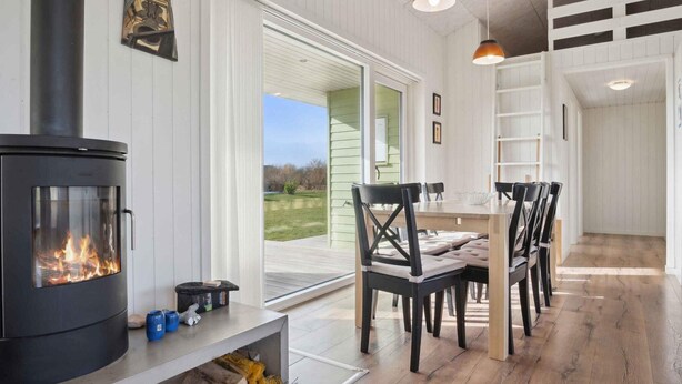 A modern interior with a wood-burning stove, a dining area with chairs, and a view through a glass door. - 5 Star Holiday Home in Sydals (Sydals)