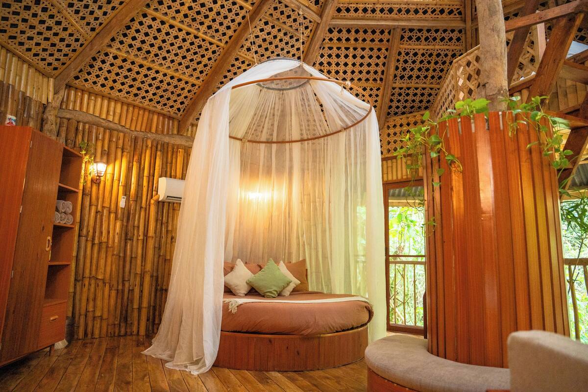 Una habitación con una cama redonda, dosel, paredes de madera y vistas al verdor.
