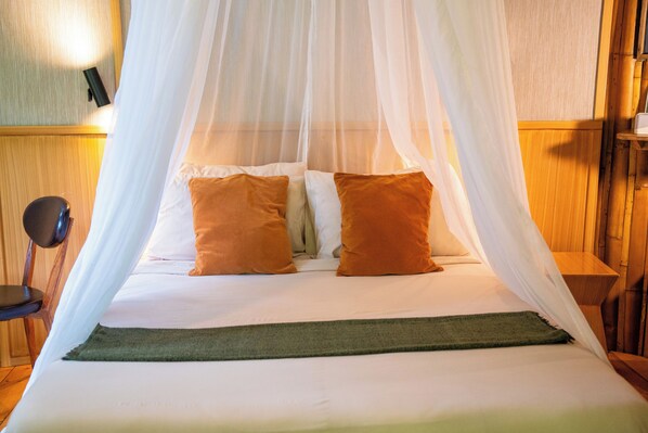 A bed with a canopy, two pillows, a bedside table, and a wall-mounted lamp.