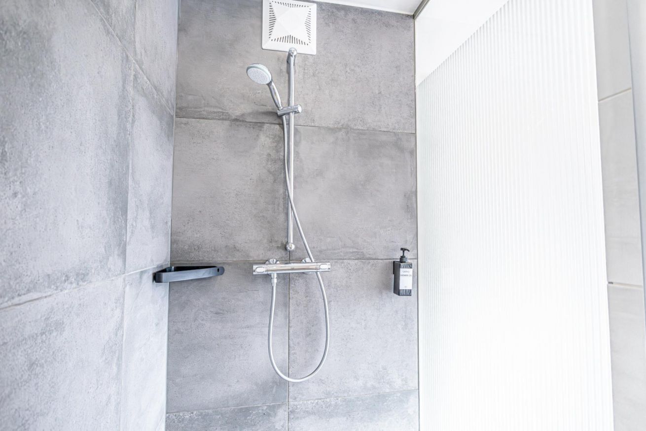 A modern shower with a handheld showerhead and a wall-mounted control panel.