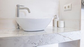 Ein Badezimmer mit einem weißen Waschtisch, einem chromfarbenen Wasserhahn, einer Marmorarbeitsplatte und einem Spiegel über dem Waschbecken.