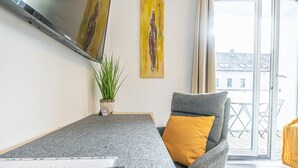 Ein modernes Wohnzimmer mit einem grauen Sofa, einem gelben Kissen, einem grauen Tisch, einer Fernbedienung und einer Topfpflanze.