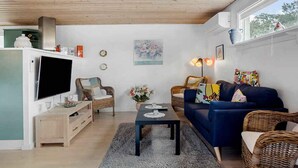 A modern living room with a flat-screen TV, wicker furniture, a blue sofa, and a large window. - 5 Star Holiday Home in Brenderup Fyn (Middelfart)