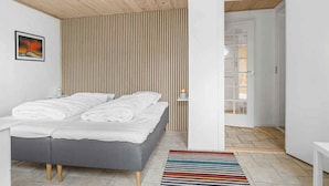 A modern bedroom with a bed, a wooden slatted wall, a colorful striped rug, and a white door leading to another room. - 5 Star Holiday Home in Brenderup Fyn (Middelfart)