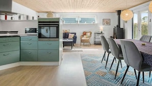 A modern kitchen with green cabinets, a microwave, and an oven. There is a dining area with a table and chairs, and a window with a view of greenery. - 5 Star Holiday Home in Brenderup Fyn (Middelfart)