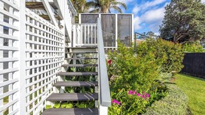 Un escalier en bois peint en blanc, doté d’une rampe en métal, est entouré d’une végétation luxuriante et de plantes en fleurs.