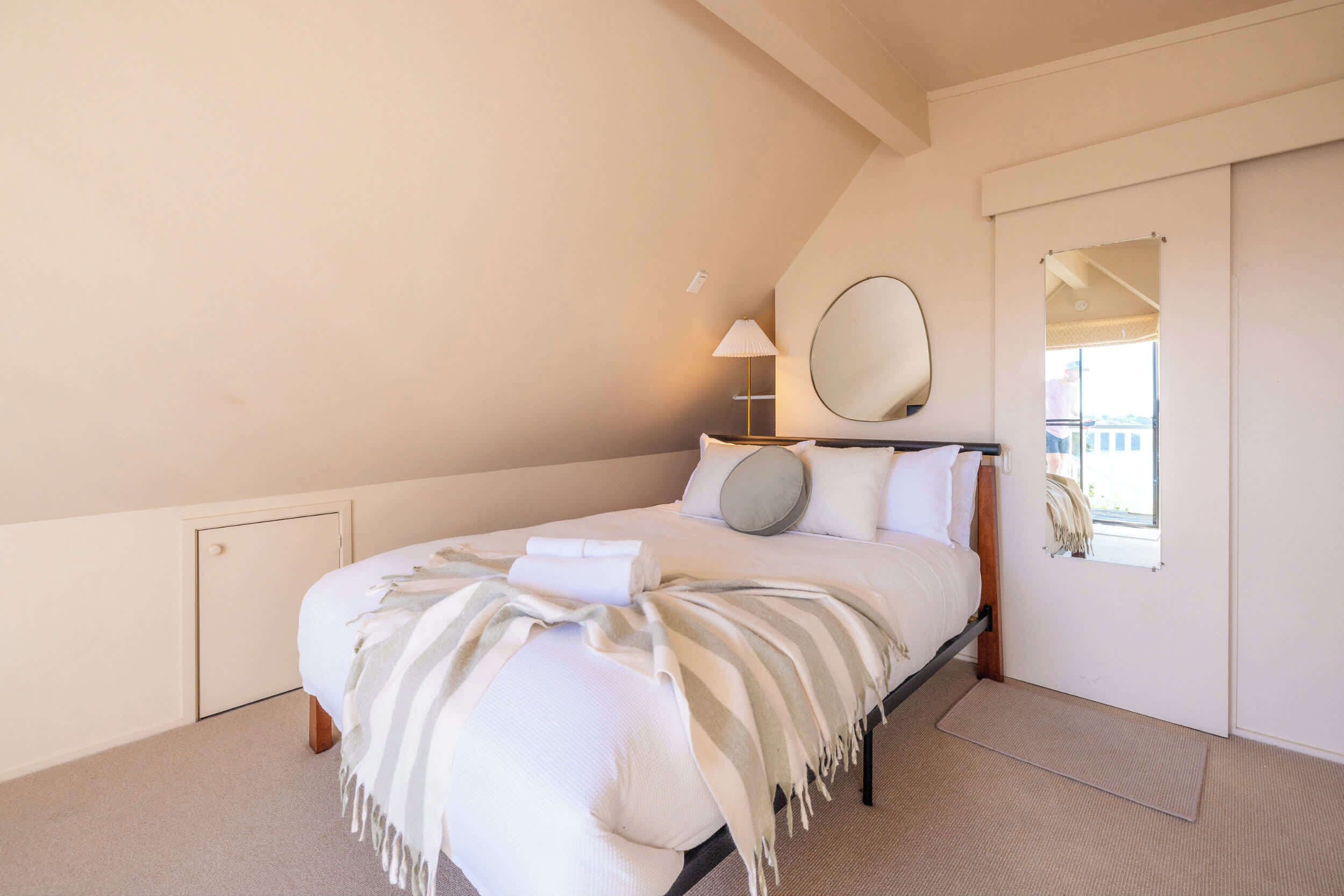A bedroom with a bed, a bedside lamp, a round mirror, and a window.