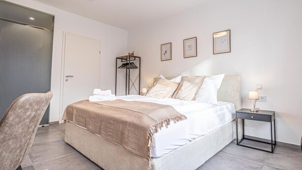 Un dormitorio con cama, mesita de noche, silla y una puerta.