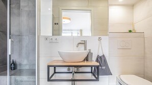 Un baño moderno con lavamanos sobre encimera, ducha e inodoro.