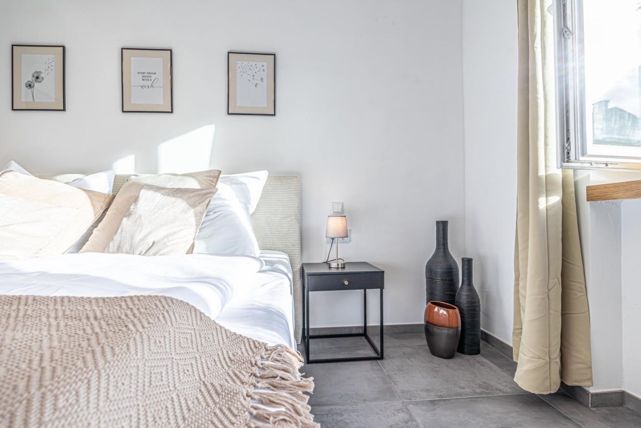 Una camera da letto ordinata con un letto, un comodino, una lampada e vasi decorativi.