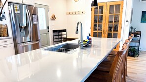 Una cocina moderna con un refrigerador de acero inoxidable, lavavajillas integrado y un comedor de madera con una barra alargada.