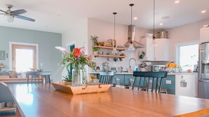 Una cocina moderna con una mesa de comedor de madera, electrodomésticos integrados e iluminación colgante.