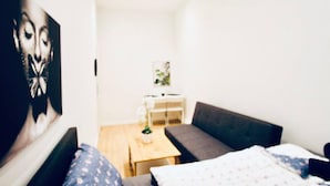 Et lille, lyst værelse med seng, to sofaer, et bord og et billede på væggen.
