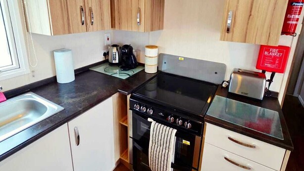 A compact kitchen with wooden cabinets, a stove, a sink, and a toaster.