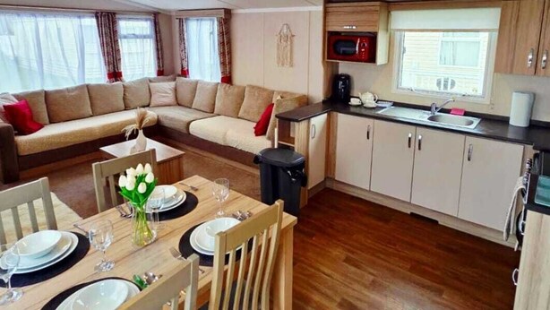 A compact living space with a dining area, kitchenette, and a sofa. - Caravan by the sea with direct access to the beach.  Pet friendly! (Barton on Sea)