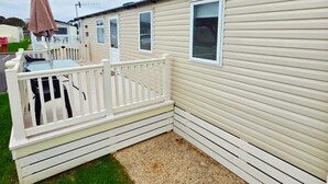 A mobile home with a fenced patio area, a small deck, and a gravel driveway. - Caravan by the sea with direct access to the beach.  Pet friendly! (Barton on Sea)