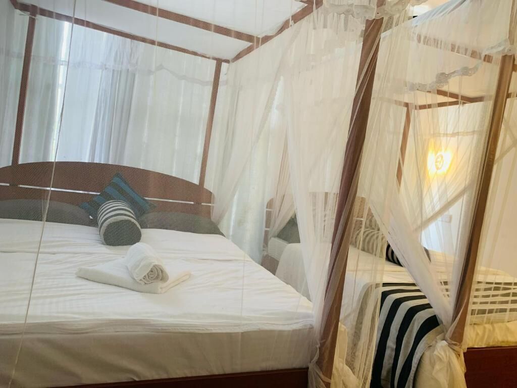 Una habitación con una cama cubierta por un dosel, una mesita de noche y una ventana con cortinas.