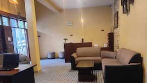 Una sala de estar con un sofá, un reposapiés y una pequeña mesa con una computadora portátil. Se ve una escalera que conduce a un nivel superior, y un balcón con vistas.