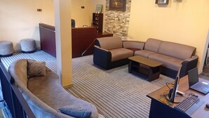 Un espacio de sala moderno con un sofá curvo, un sofá modular y una mesa de centro. Hay un escritorio con una computadora portátil y un ratón. El cuarto tiene piso a rayas y una pared de acento de piedra.
