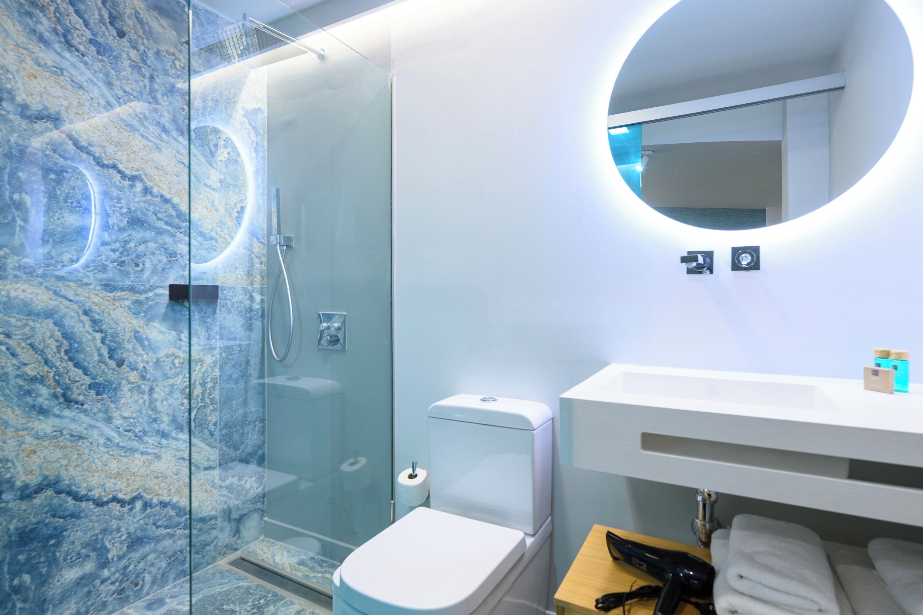 Un baño moderno con ducha envuelta en vidrio, inodoro blanco y espejo redondo sobre un lavabo blanco.