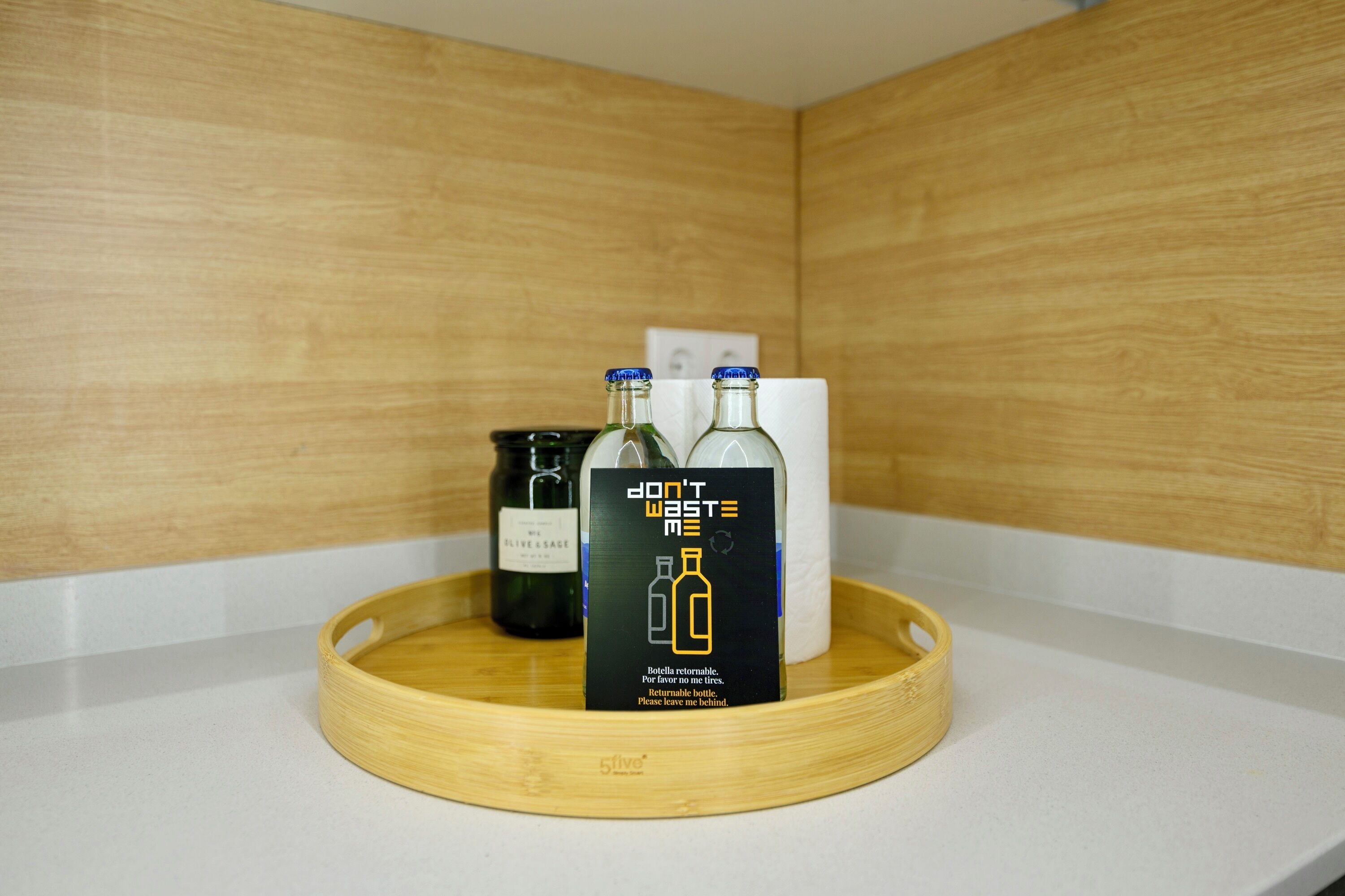Un plateau en bois avec trois bouteilles posées sur un comptoir blanc.