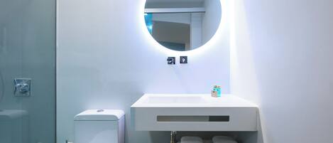 A modern bathroom with a round mirror, white sink, and neatly folded towels on a wooden shelf.