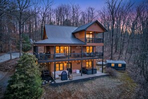 Une cabane en rondins à deux étages, dotée d’un balcon, d’un espace salon extérieur et d’un coin barbecue.