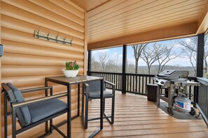 Une terrasse extérieure couverte, équipée d’un barbecue, de sièges et offrant une vue sur les arbres.