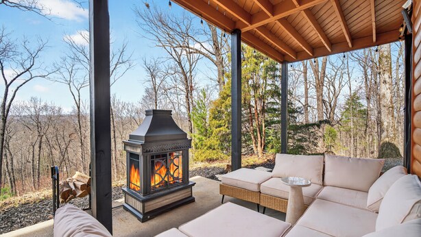 Un espace extérieur abrité, doté d’un poêle à bois, de canapés confortables et offrant une vue sur la forêt environnante.