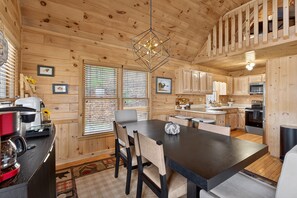 A wooden cabin interior with a dining area, kitchen, and a staircase.