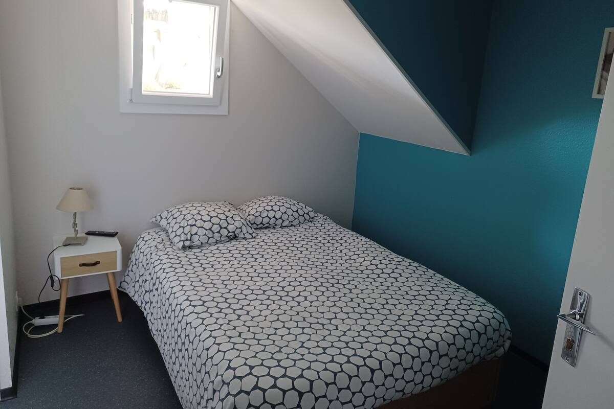 A bedroom with a bed, a nightstand, a lamp, and a window.